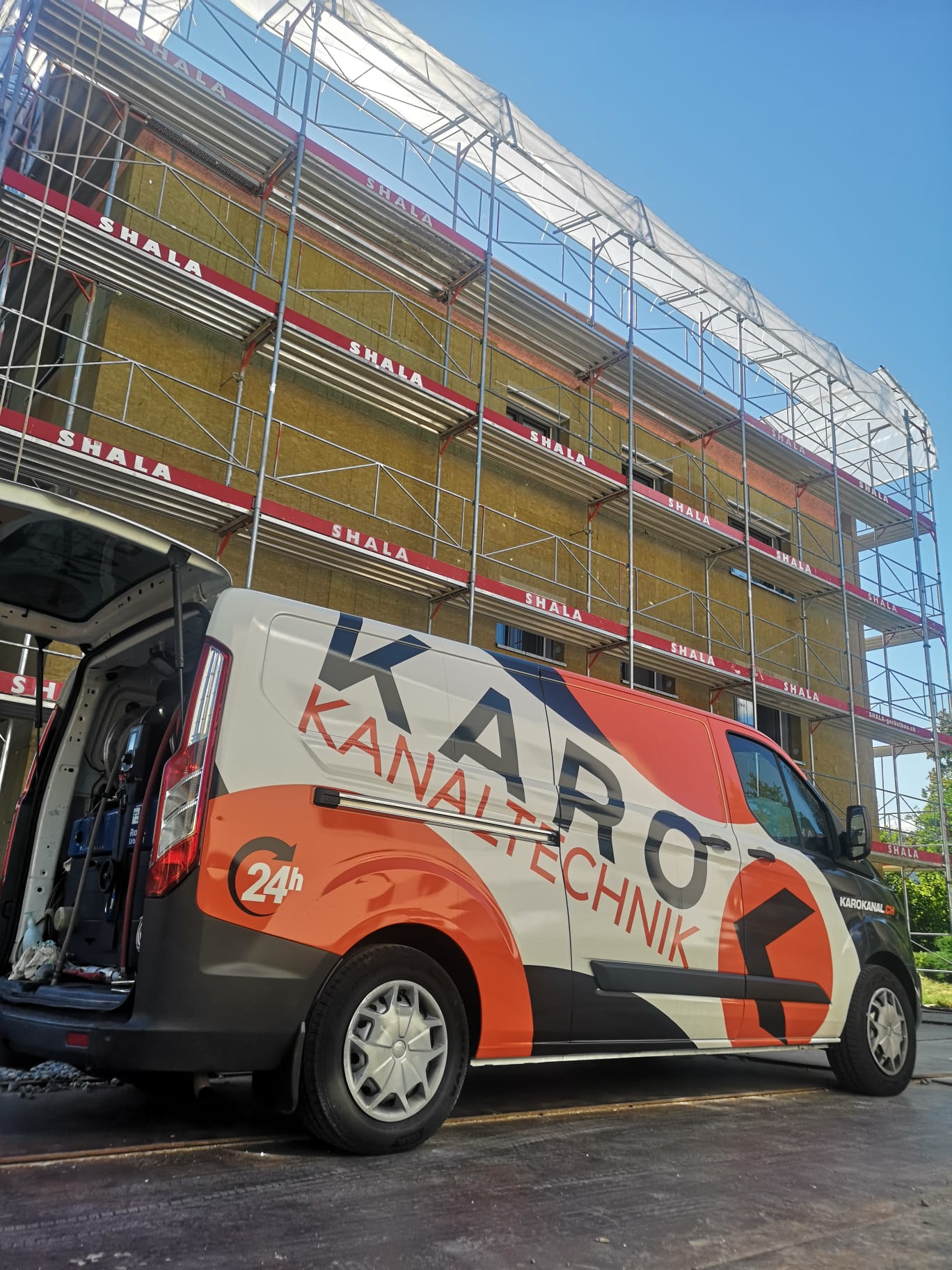 Kanalarbeiten an einem eingerüsteten Neubau – Einsatzfahrzeug mit offener Heckklappe